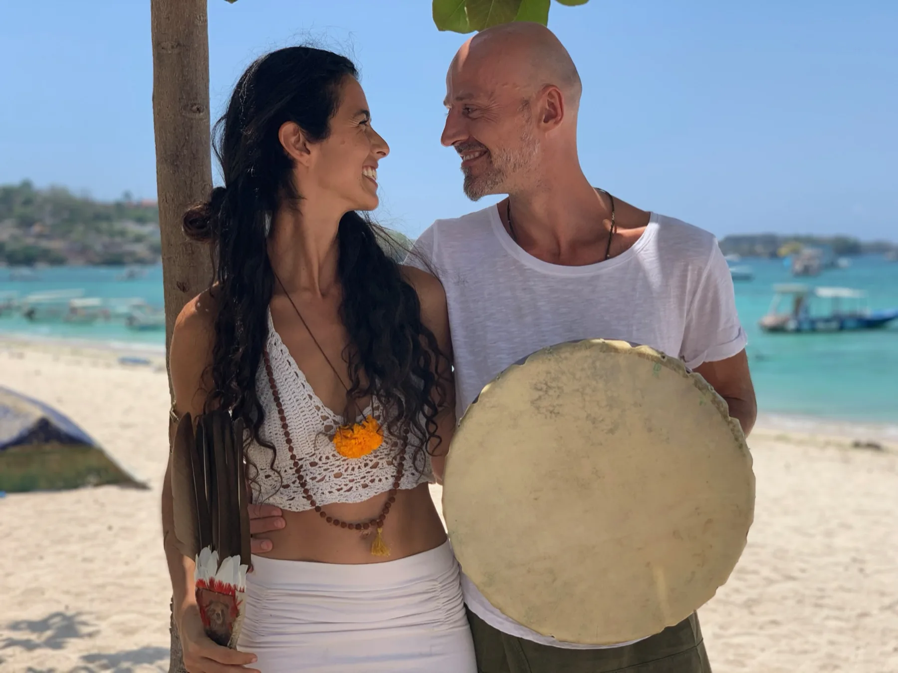 Marcela and Tobias on the beach, laughing, with a frame drum